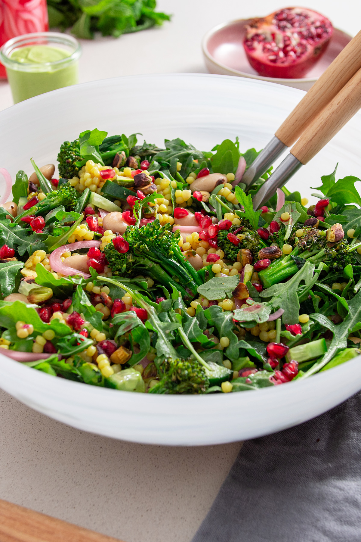 Close-up of grilled broccolini and pomegranate salad showing details of pomegranate seeds, pistachios, and butter beans mixed with fresh greens.