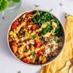 Moroccan-inspired nourish bowl with a creamy sauce drizzled on top, next to golden cutlery on a yellow napkin.