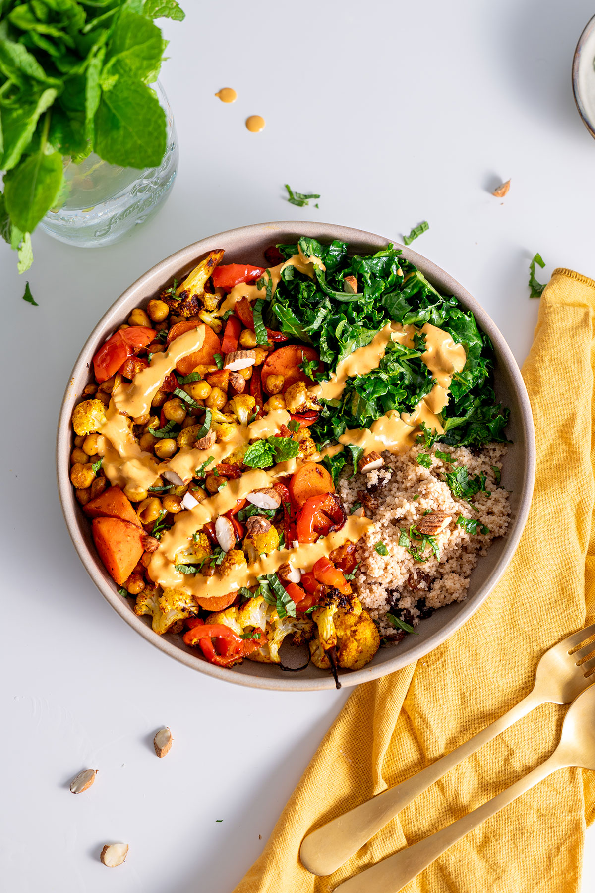 Moroccan-inspired nourish bowl with a creamy sauce drizzled on top, next to golden cutlery on a yellow napkin.