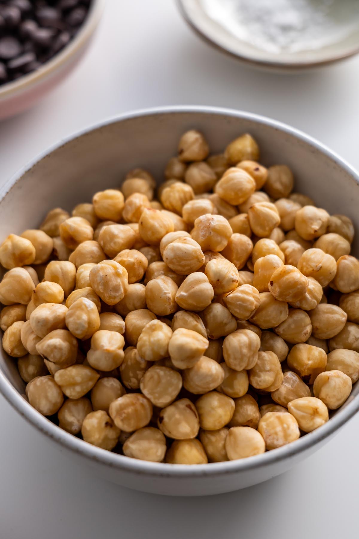 Close-up of blanched hazelnuts in a white bowl on a light background.