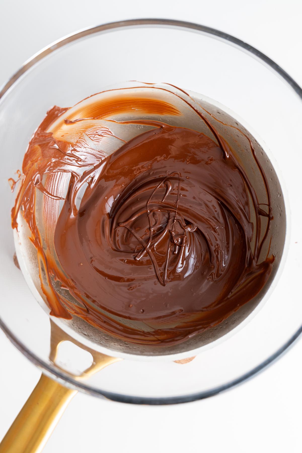 Melted dark chocolate in a glass mixing bowl with a spatula.