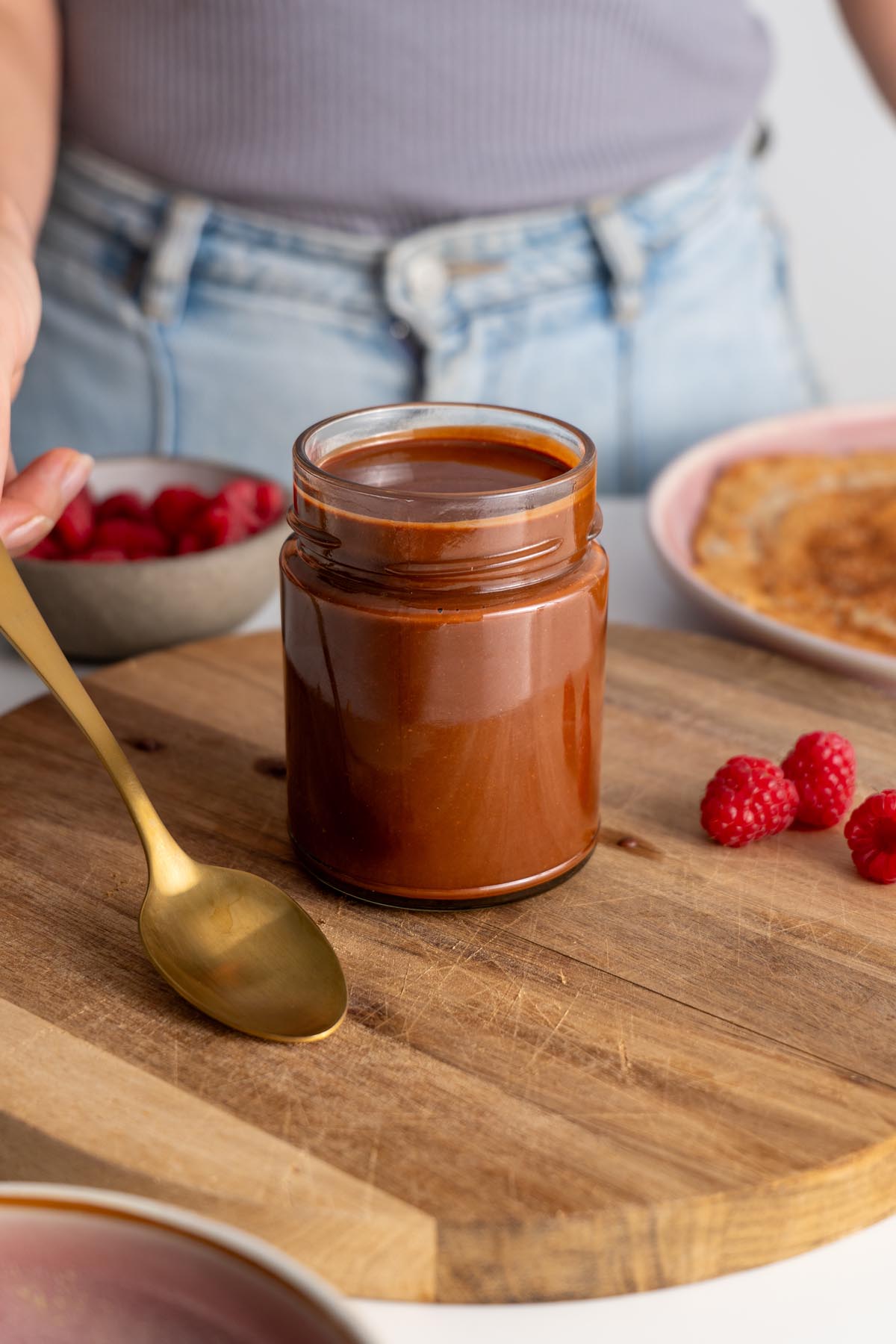 Vegan chocolate spread in a jar on a wooden surface with raspberries.