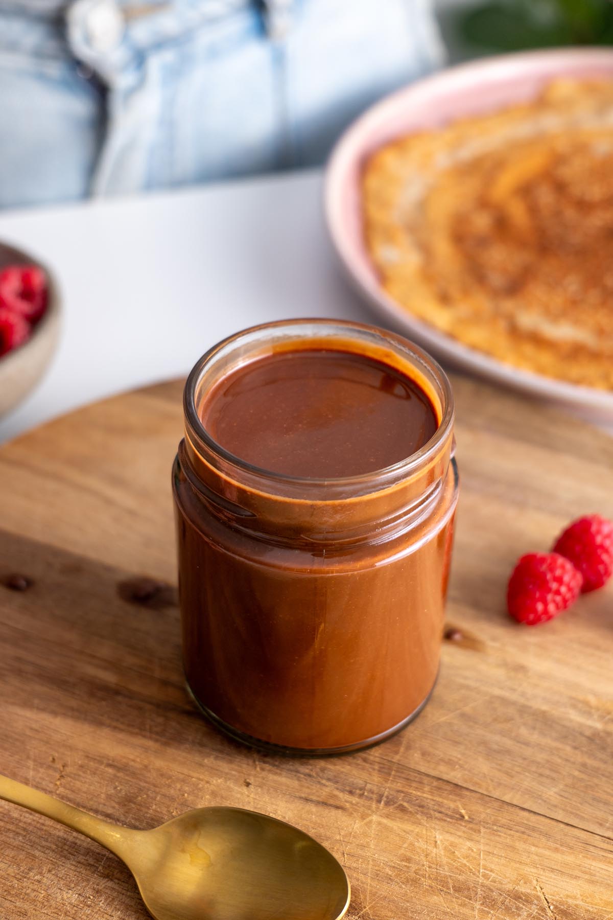 Vegan chocolate spread in a jar closeup on a wooden surface with raspberries.