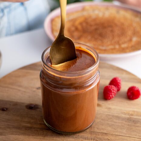 Scooping vegan chocolate spread from a jar with a golden spoon.