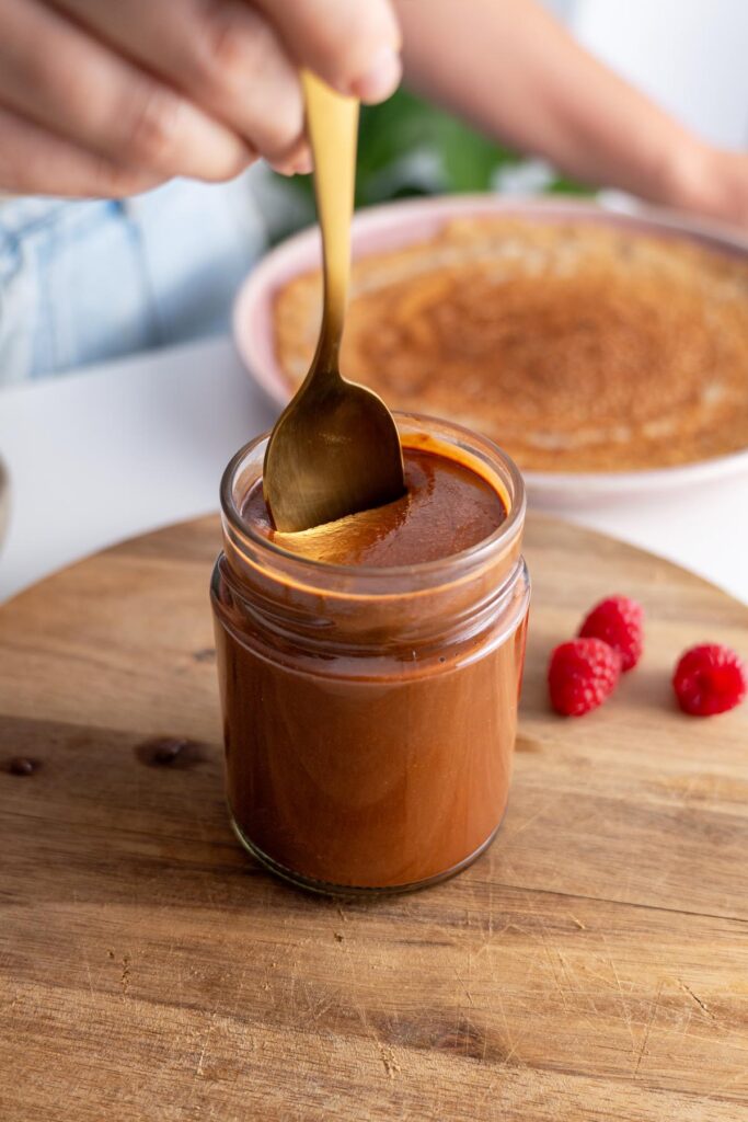 Scooping vegan chocolate spread from a jar with a golden spoon.