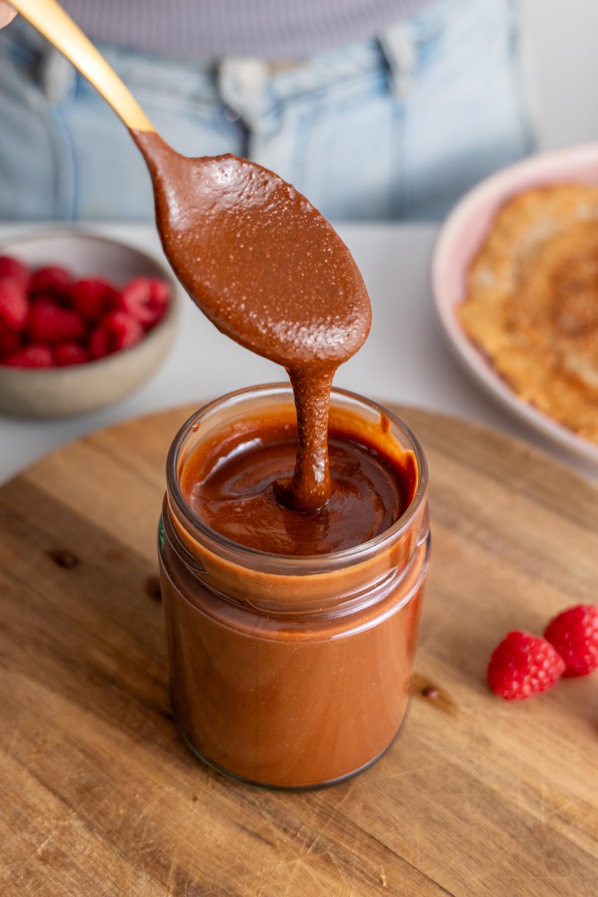 Vegan chocolate spread dripping from a spoon into a glass jar.