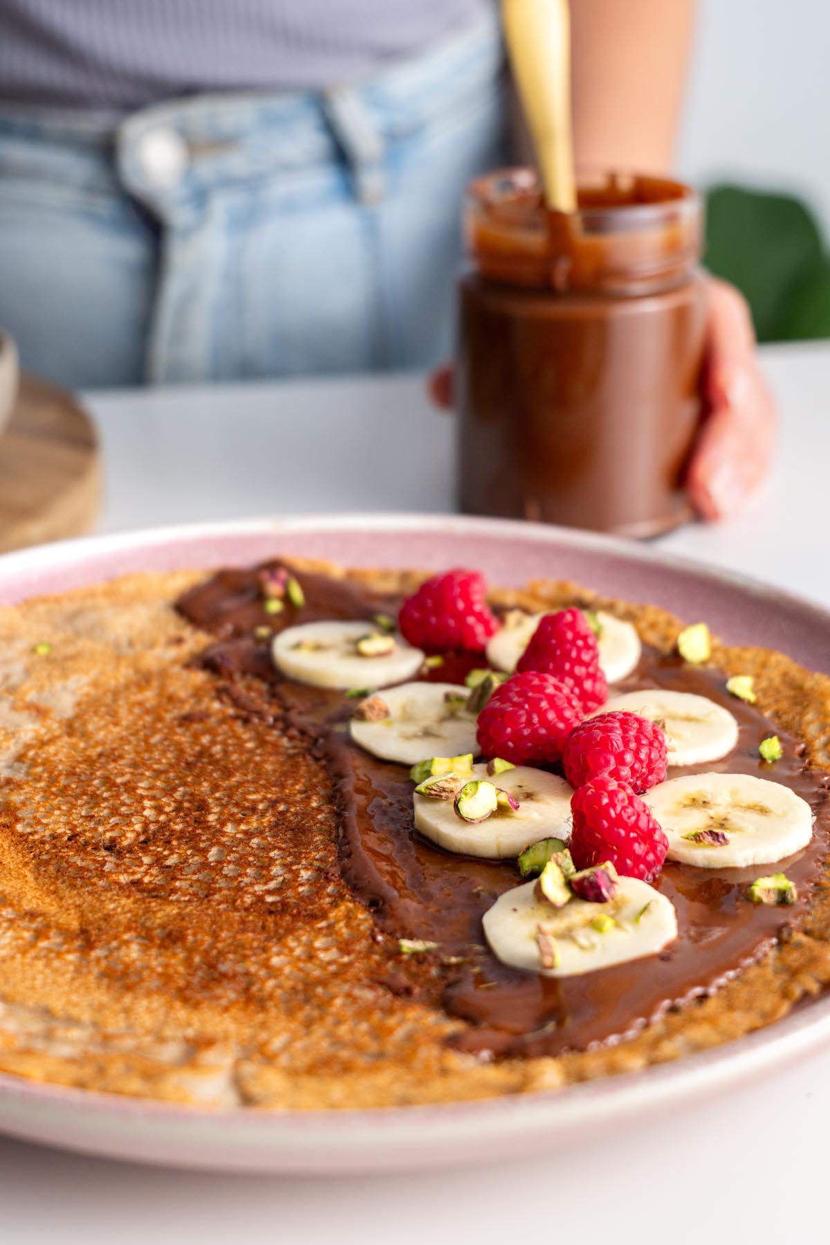 Vegan chocolate spread on a crepe garnished with banana slices and raspberries.