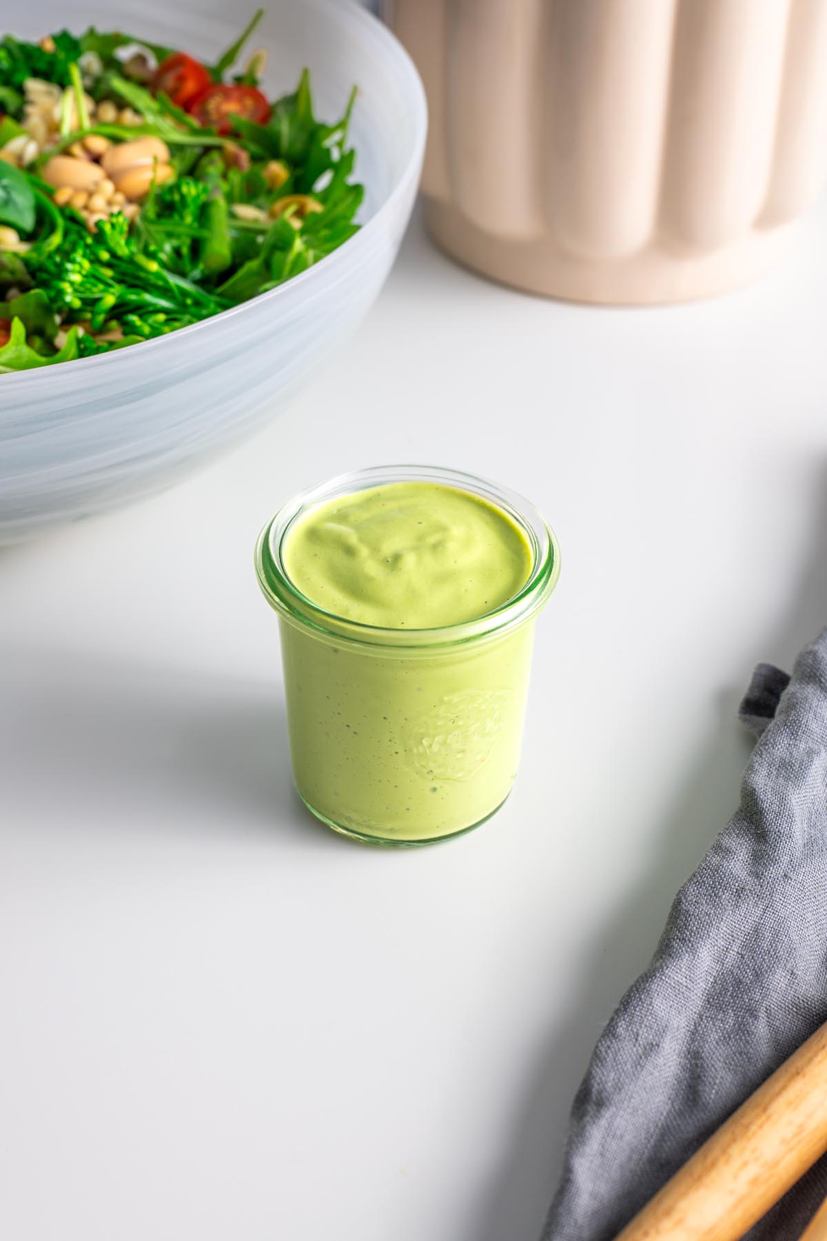 Vibrant green healthy salad dressing in a jar in front of a pesto orzo salad