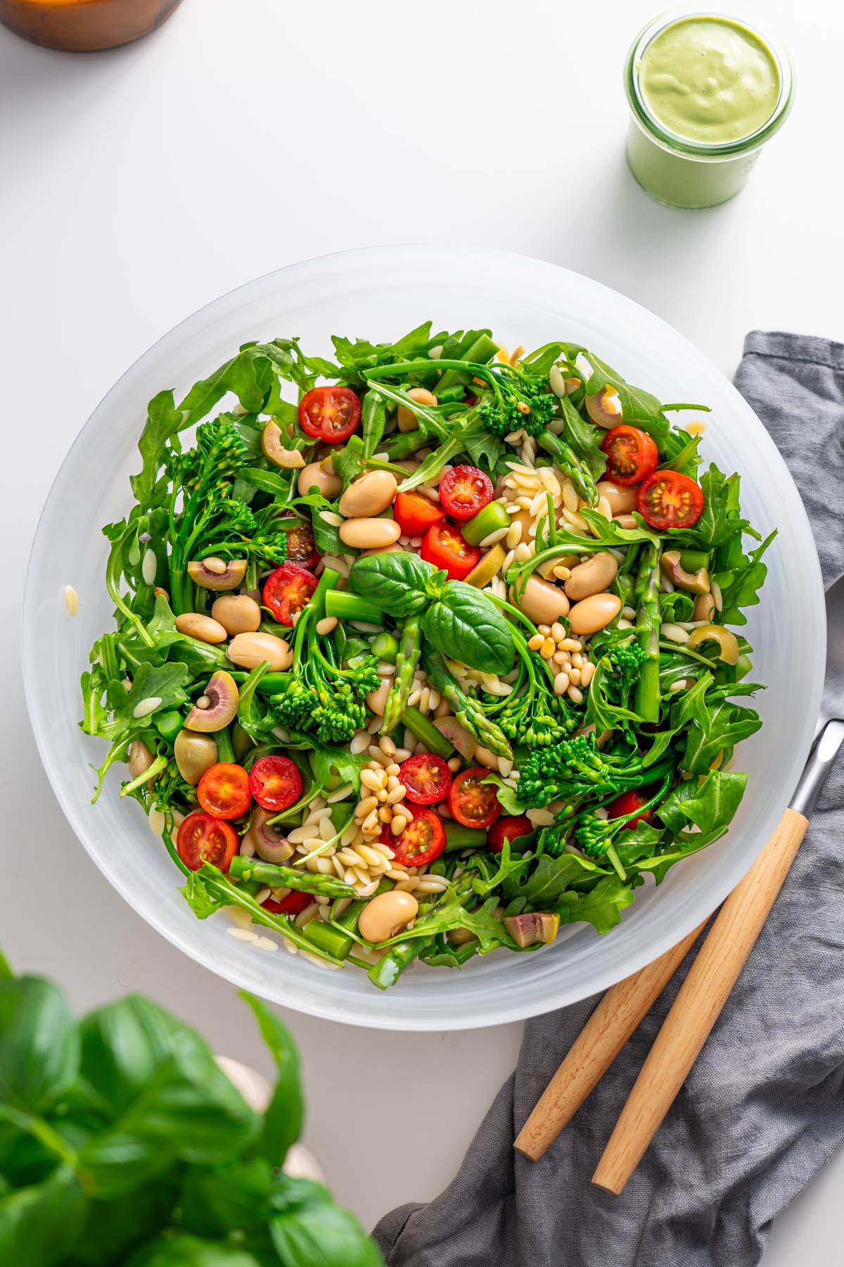 Top view of freshly prepared Pesto Orzo Salad in a white bowl on a kitchen counter, featuring arugula, broccolini, and cherry tomatoes.
