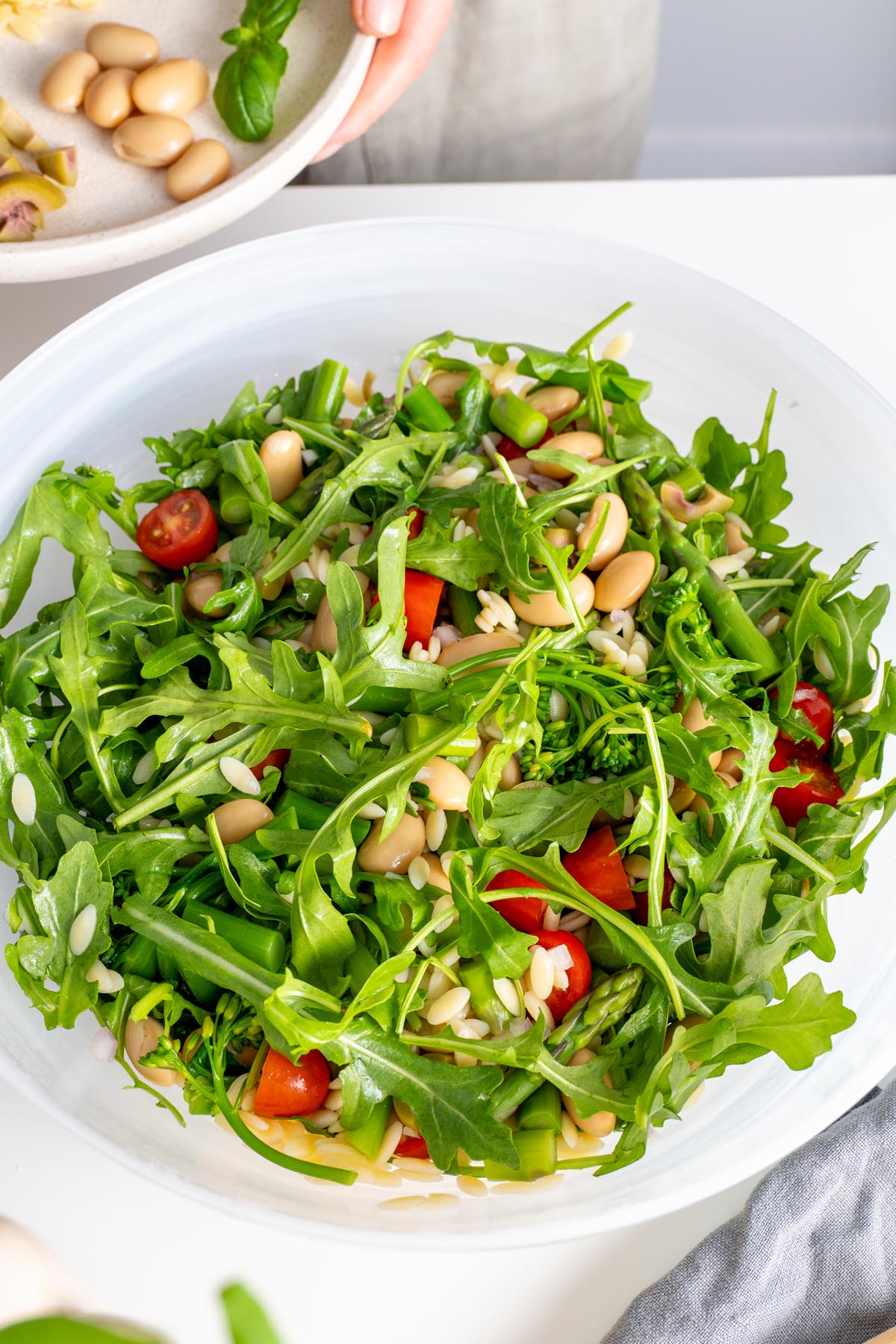 Detailed top view of a freshly tossed bowl of Pesto Orzo Salad, emphasizing the textures and vibrant colors of the fresh ingredients.