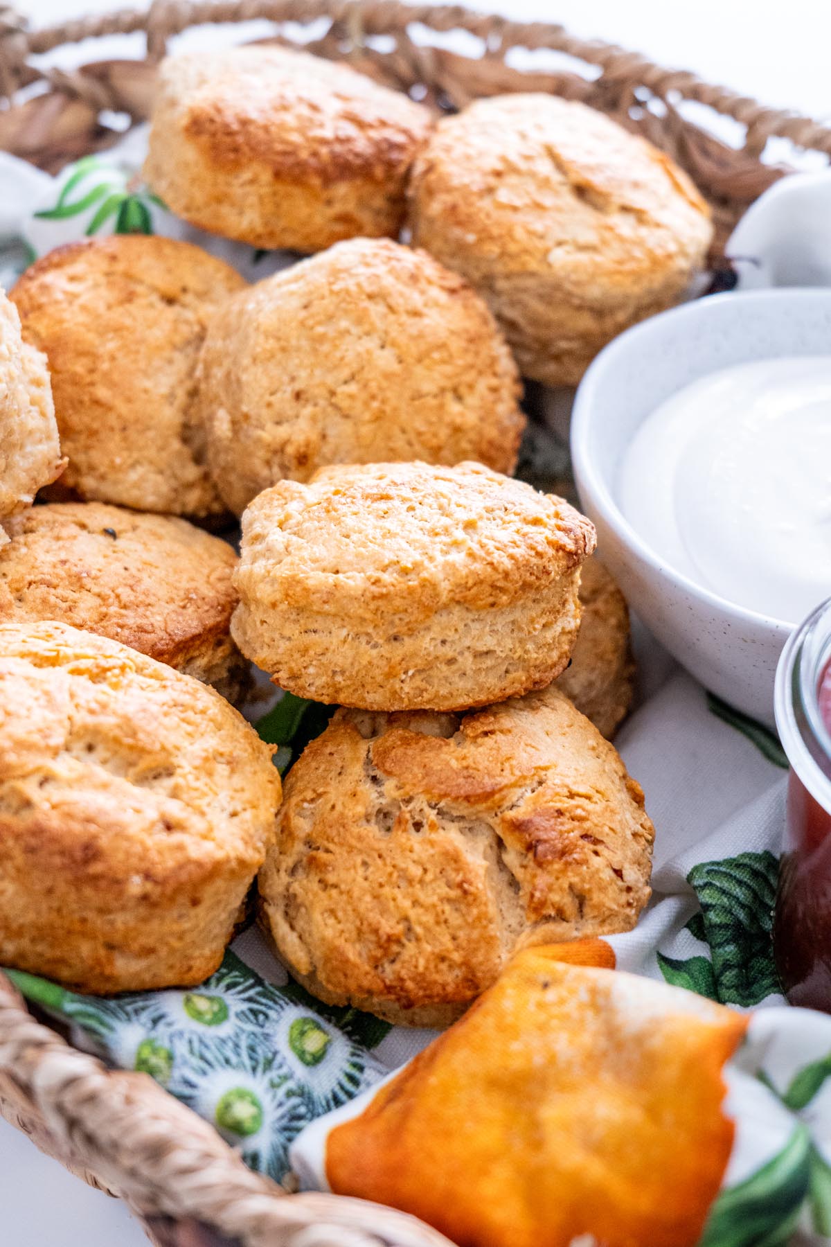 A basket of freshly baked vegan scones with cream and jam on a colorful cloth.