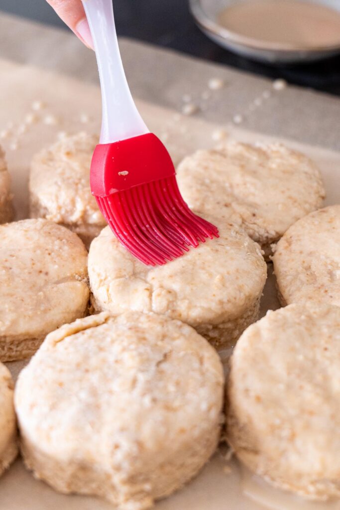Vegan scones arranged on a baking sheet being brushed with vegan egg wash