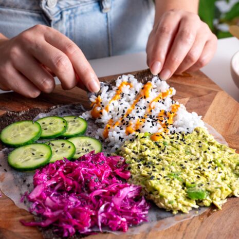 Hands folding a colorful veggie sushi wrap filled with fresh ingredients