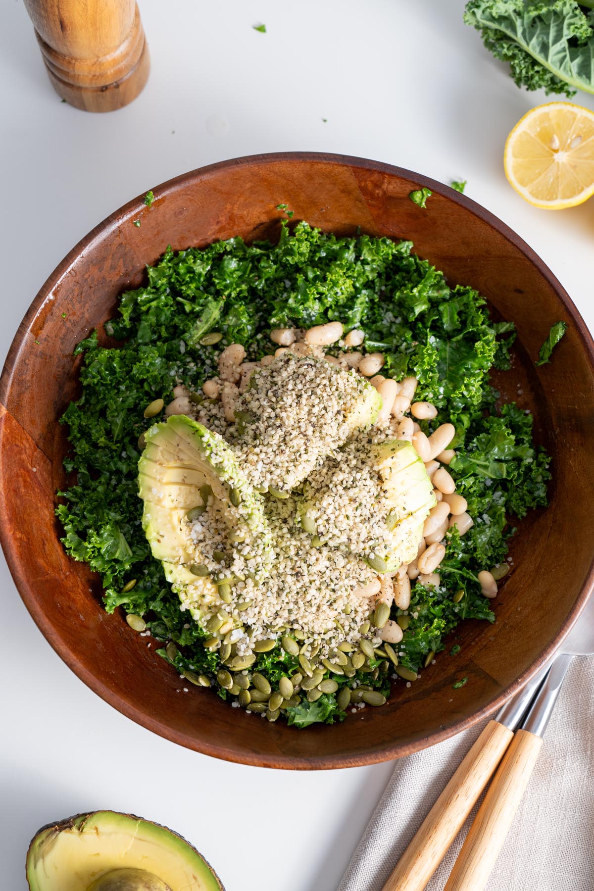 Erewhon kale salad in a wooden bowl with hemp seeds, pumpkin seeds, and avocado on top, ready to be tossed.