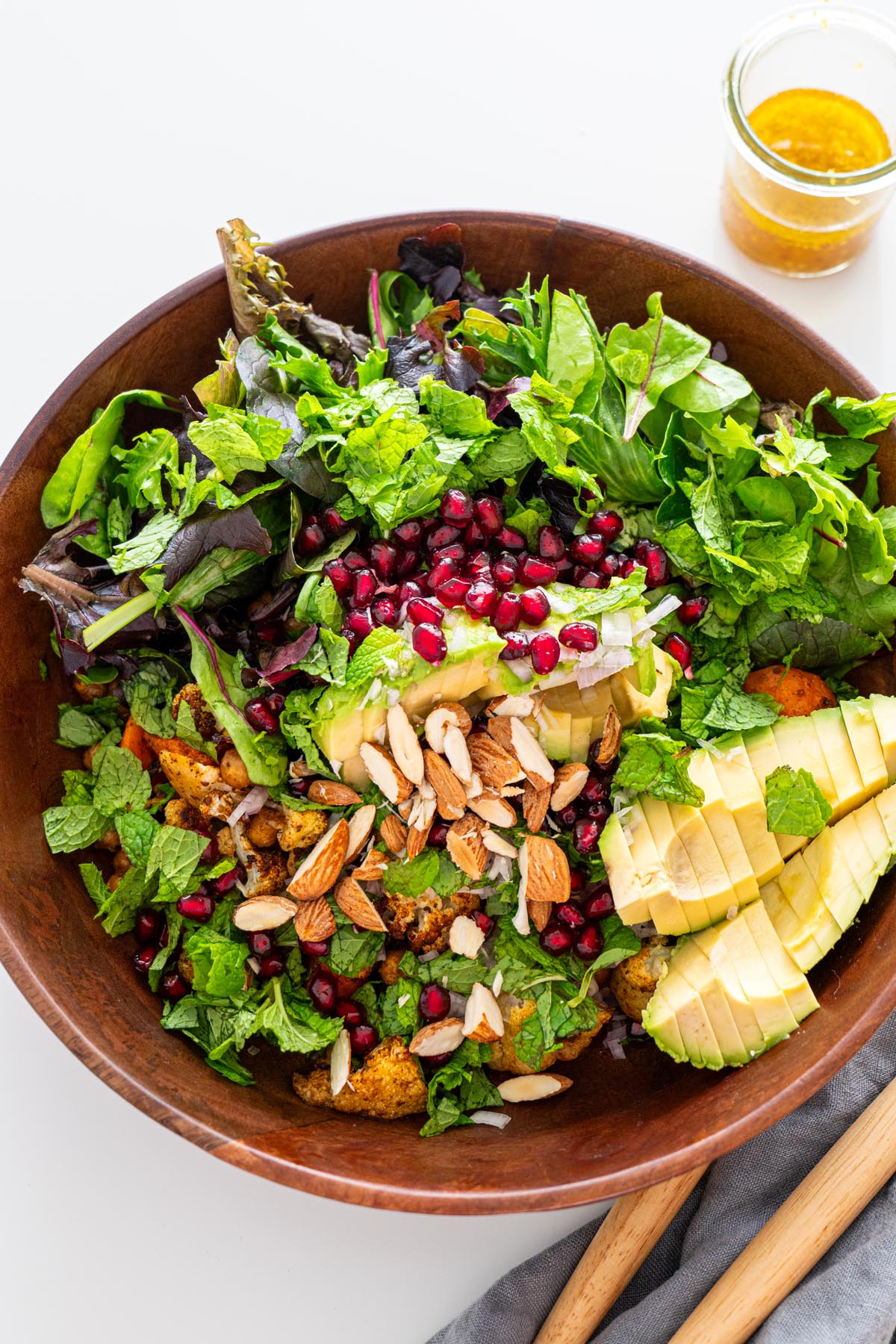 Freshly made spiced roasted cauliflower and chickpea salad in a wooden bowl with avocado, almonds, pomegranate seeds, and mint.