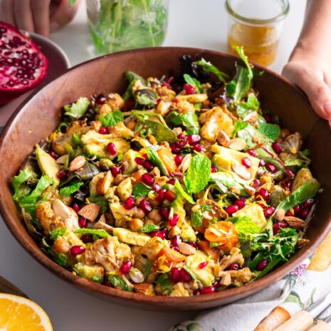 Close-up of spiced roasted cauliflower and chickpea salad in a wooden bowl with fresh ingredients.