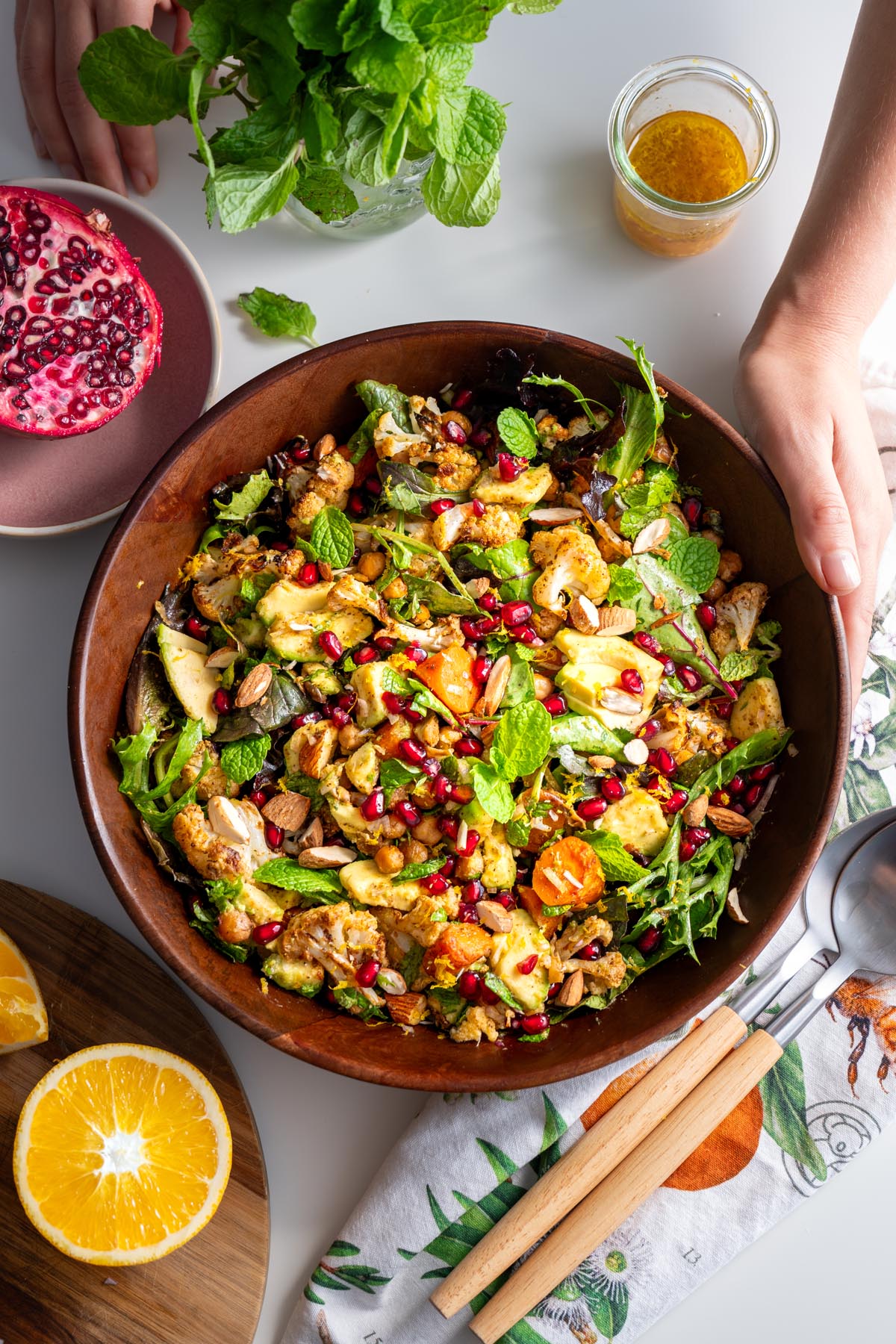 Top view of a colorful spiced roasted cauliflower and chickpea salad in a wooden bowl with dressing on the side.