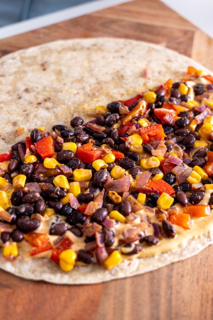 Tortilla with black bean mixture and cashew queso spread on a cutting board