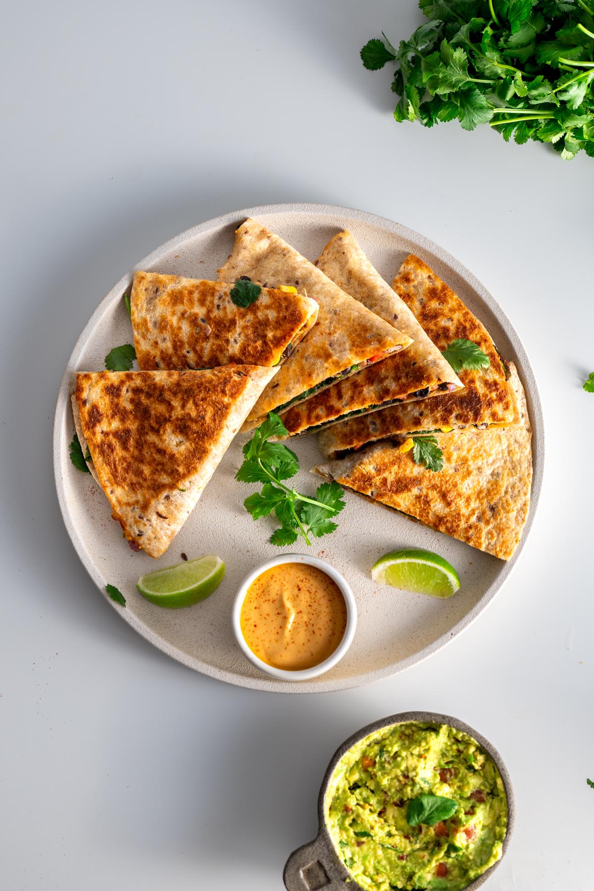 Overhead view of sliced quesadillas with lime wedges and dipping sauce.