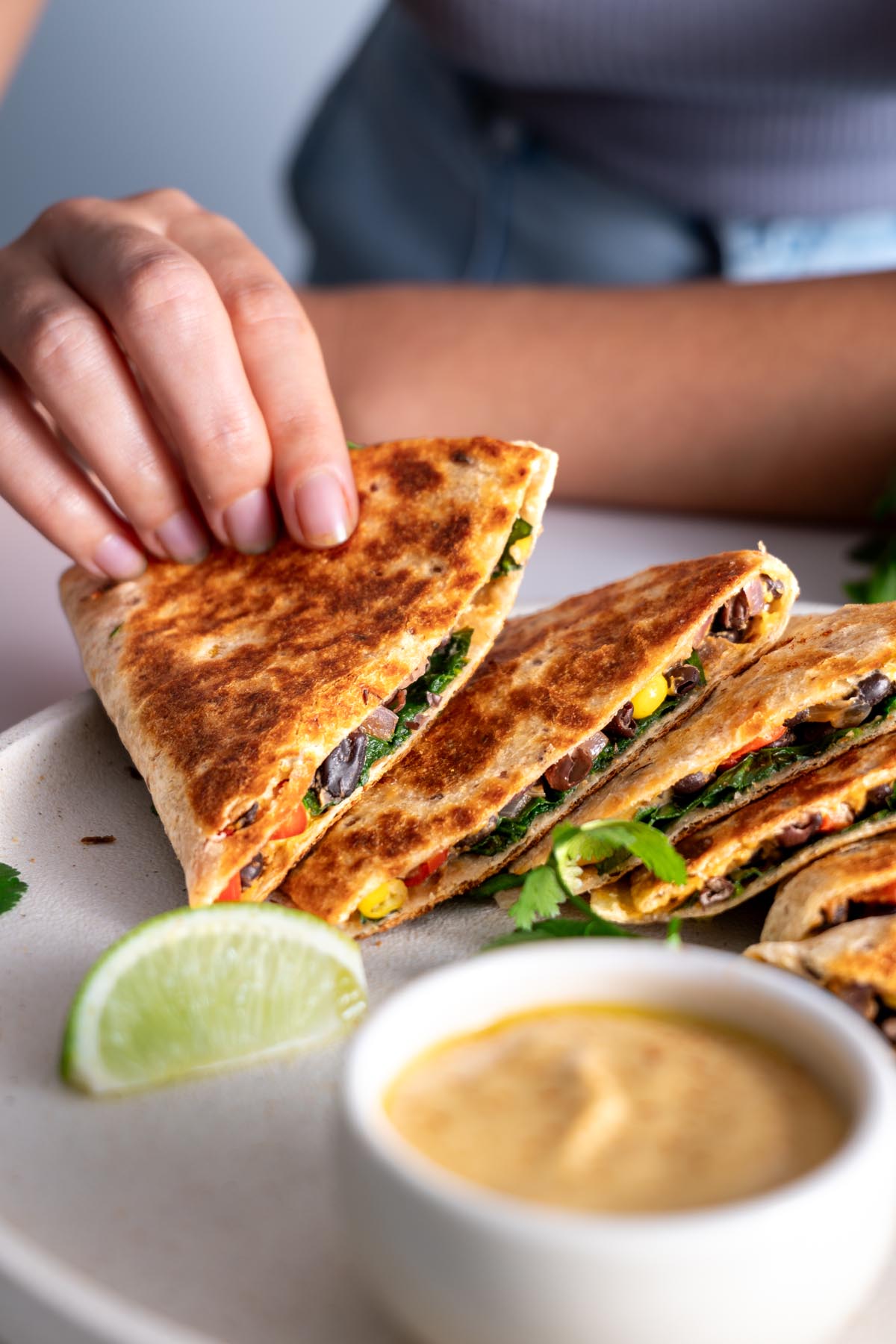 Close-up of a hand holding a slice of quesadilla with dipping sauce in the foreground.