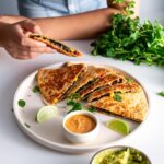 Sarah Cobacho of plantbaes picking up a slice of black bean quesadilla from a plate.