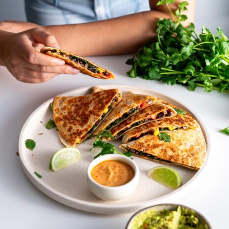 Sarah Cobacho of plantbaes picking up a slice of black bean quesadilla from a plate.