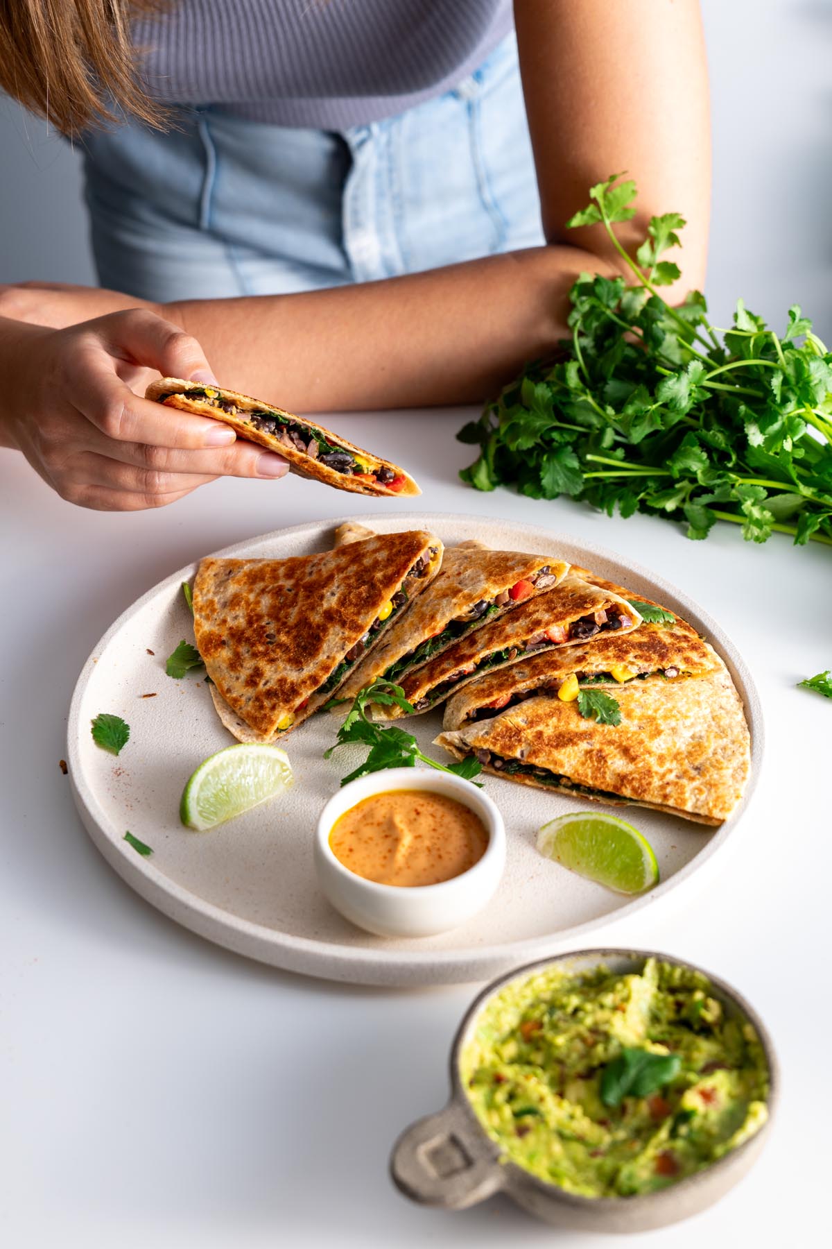 Sarah Cobacho of plantbaes picking up a slice of black bean quesadilla from a plate.