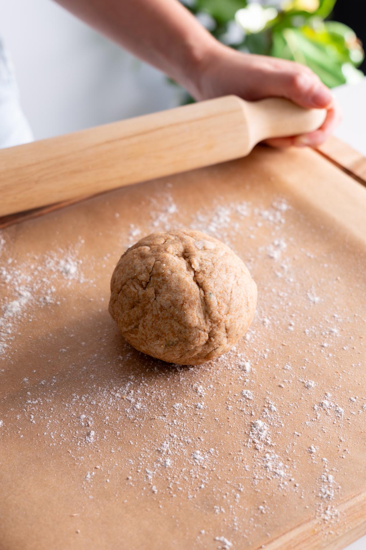 Hands rolling out dough with a rolling pin on a floured surface.