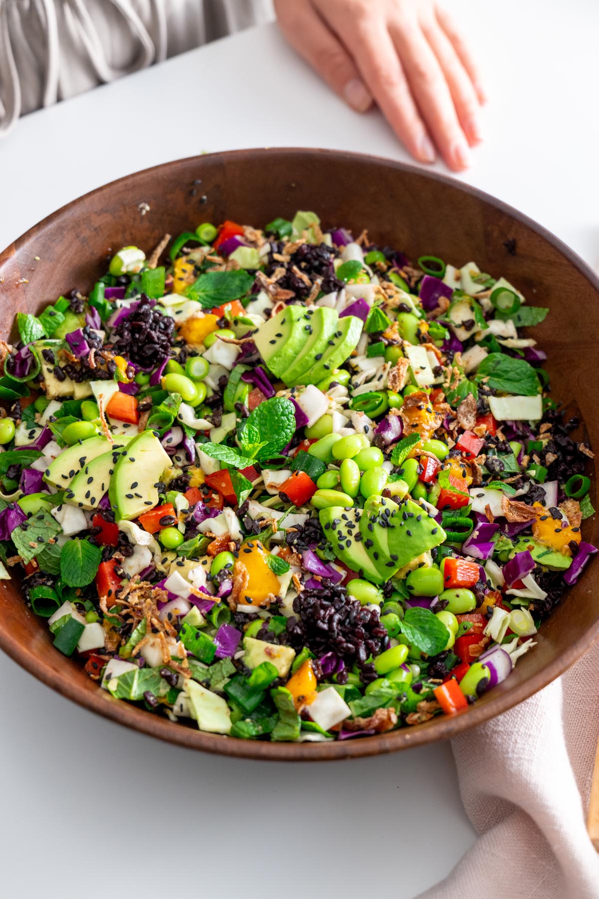 Bowl of colorful salad ingredients, including edamame, red bell pepper, cabbage, mango, avocado, mint, green onions, and black sesame seeds.