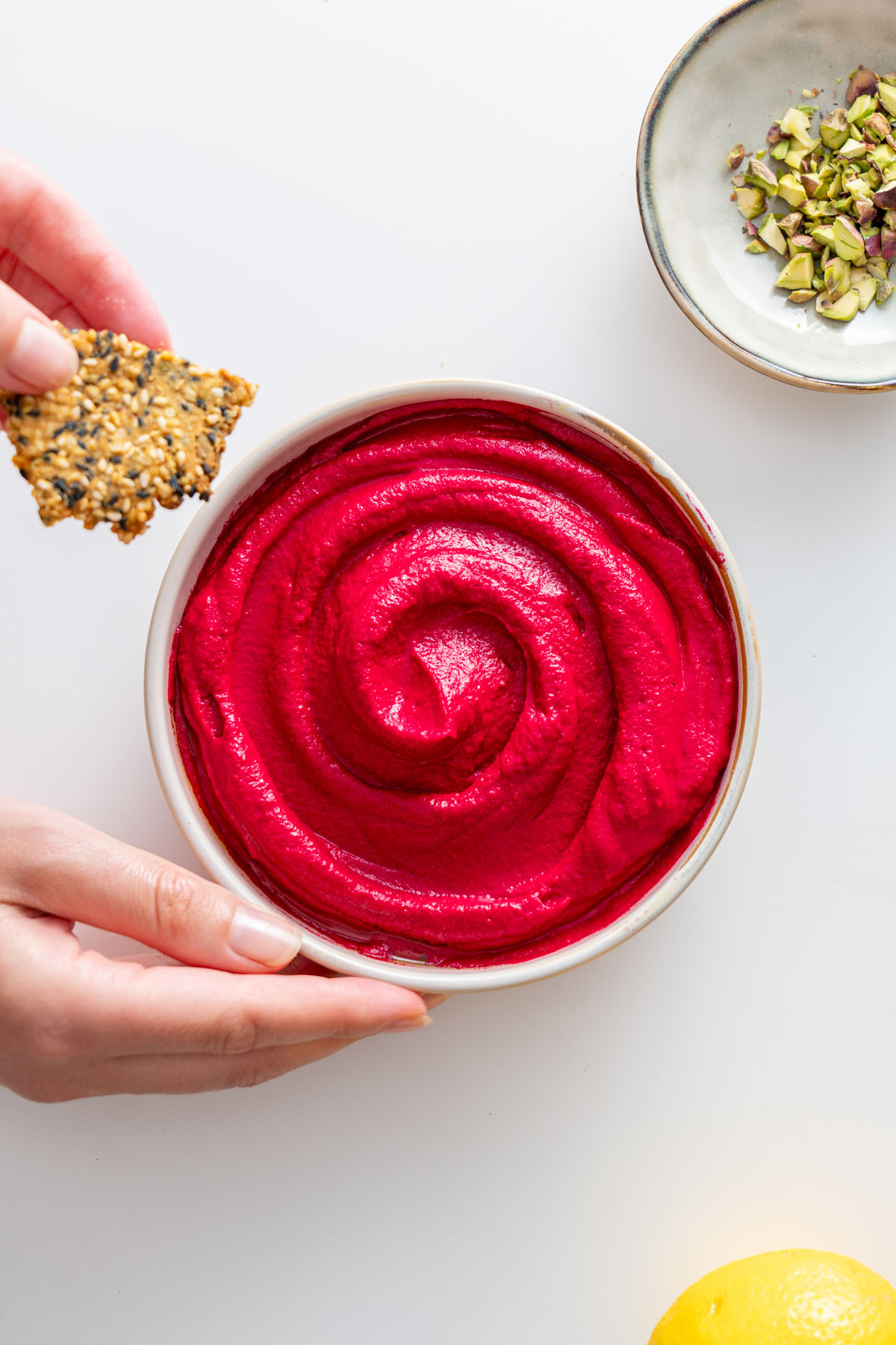 Sarah Cobacho holding a seed cracker over a bowl of beetroot hummus.