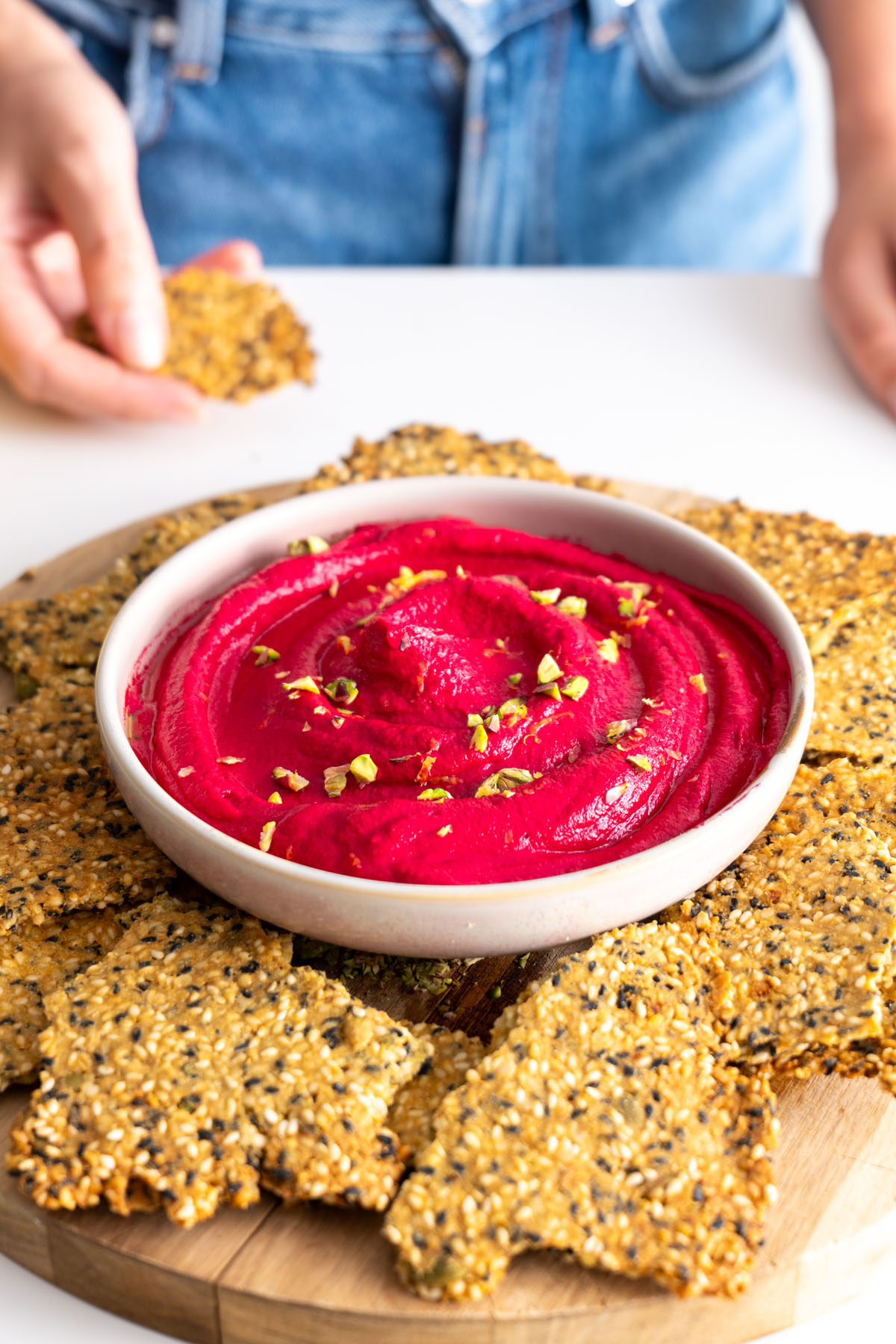Beetroot hummus topped with chopped pistachios and surrounded by crackers.