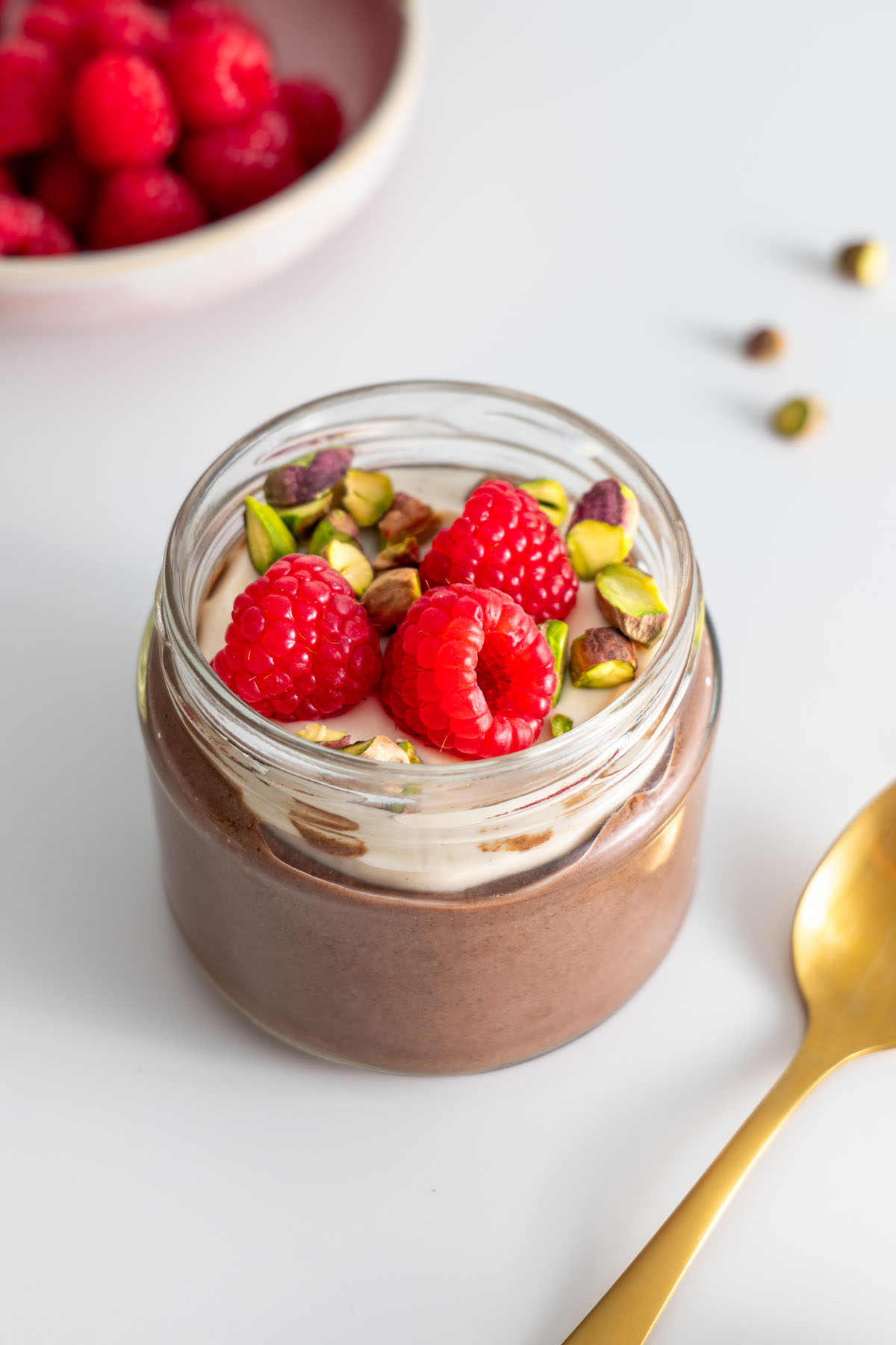 Cacao chia pudding topped with soy yogurt, raspberries, and pistachios in a glass jar.