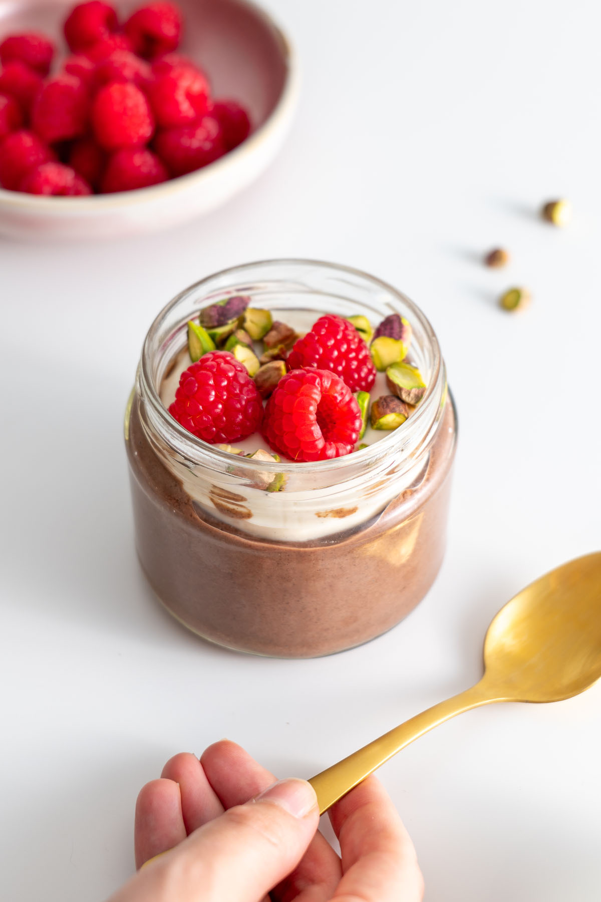Sarah holding a golden spoon next to a jar of cacao chia pudding with toppings.