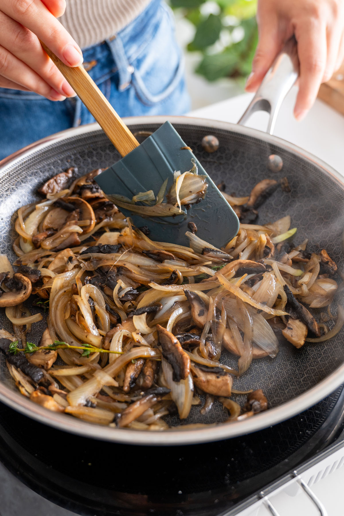 Stirring caramelized onion and mushroom mixture in a pan with a spatula.