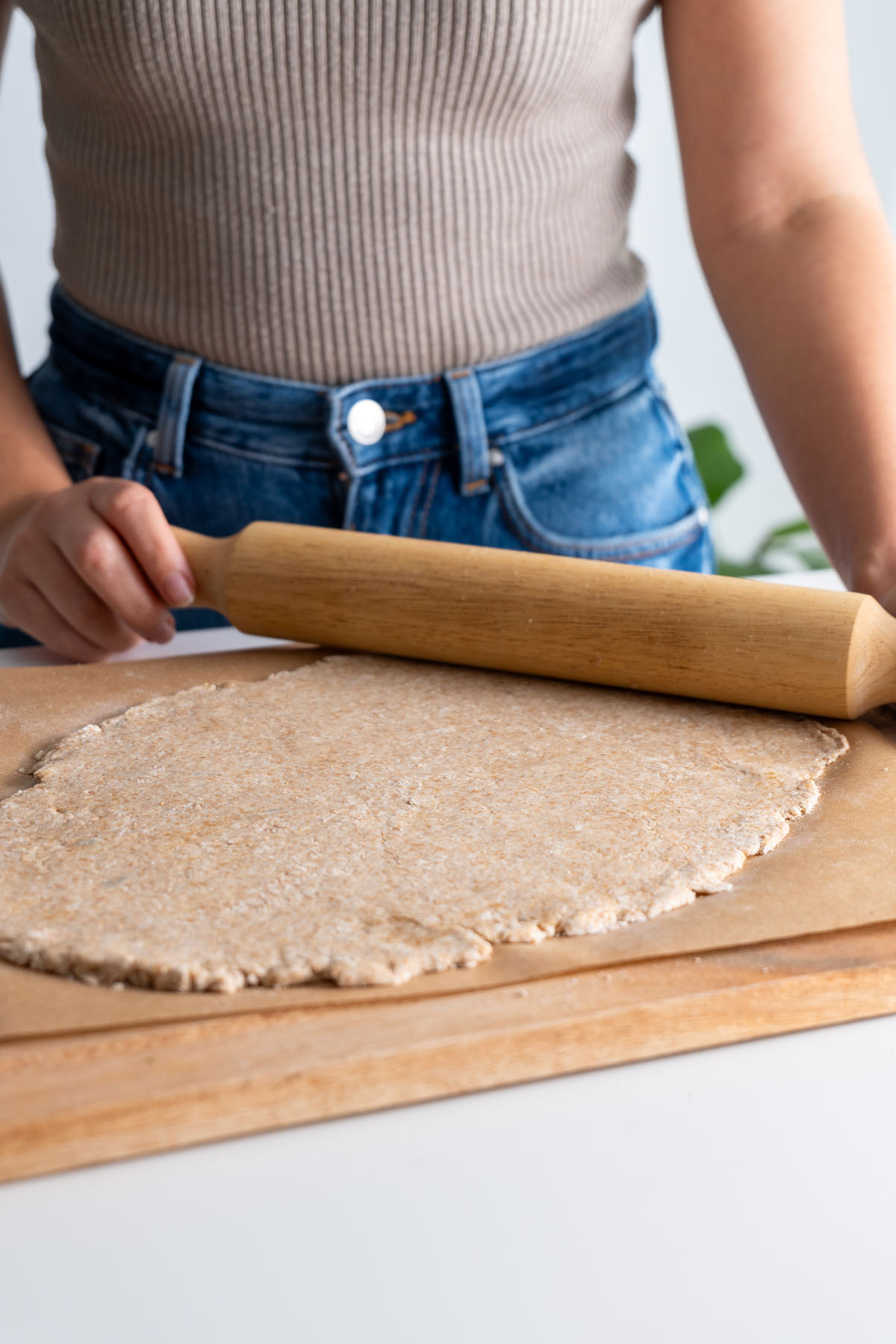 Flattening wholemeal spelt flour dough with a rolling pin on a parchment paper surface.
