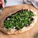 Galette topped with fresh arugula, plant-based feta, and balsamic glaze.