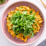 Creamy high protein pumpkin pasta served in a pink bowl, topped with fresh rocket