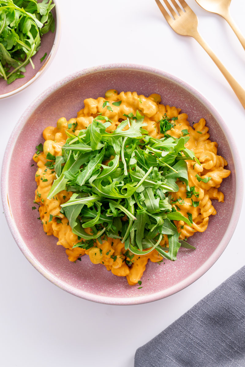 Creamy high protein pumpkin pasta served in a pink bowl, topped with fresh rocket
