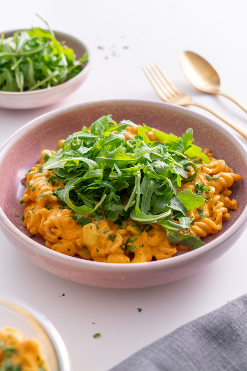 Creamy high protein pumpkin pasta served in a pink bowl, topped with fresh rocket