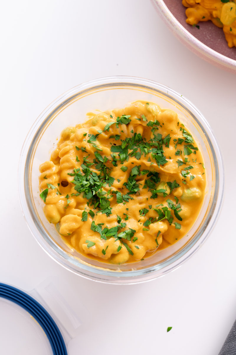 Creamy high protein pumpkin pasta in a glass container, topped with chopped parsley