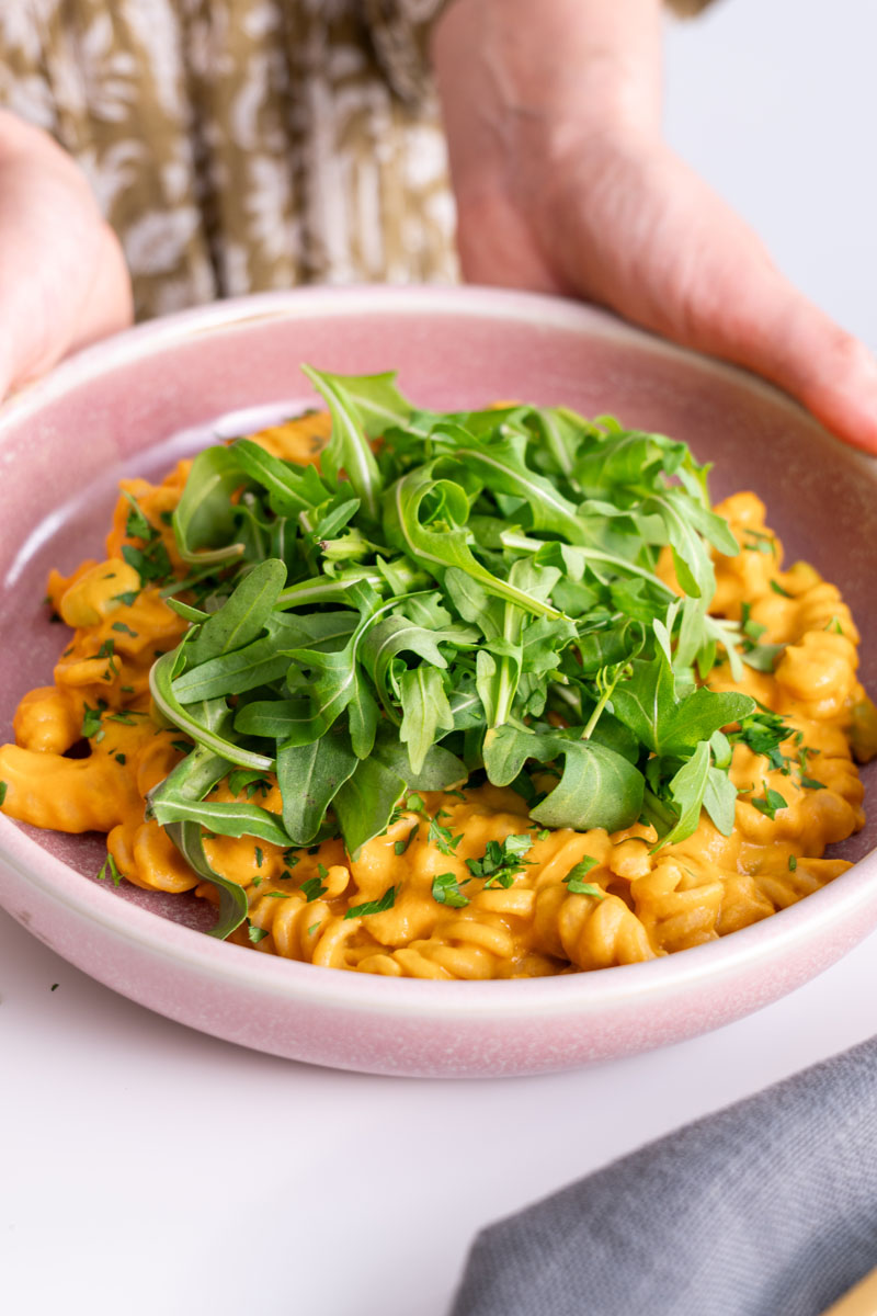 Sarah Cobacho holding a pink bowl of pumpkin pasta garnished with fresh rocket