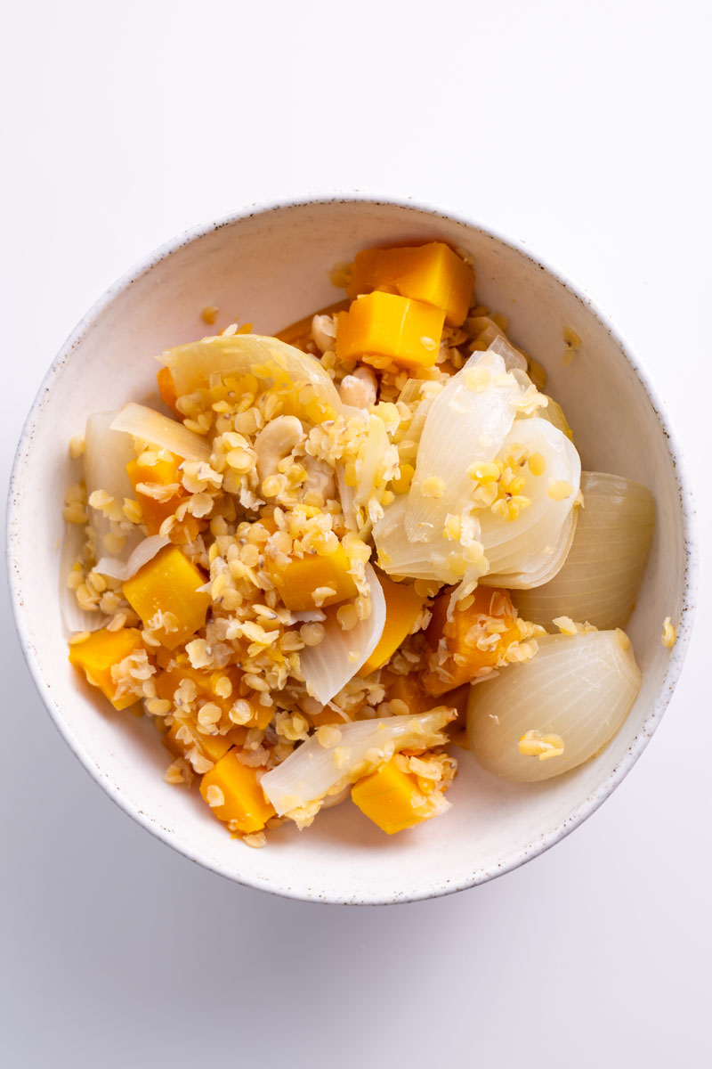 A close-up of cooked pumpkin, onion, and red lentils in a bowl