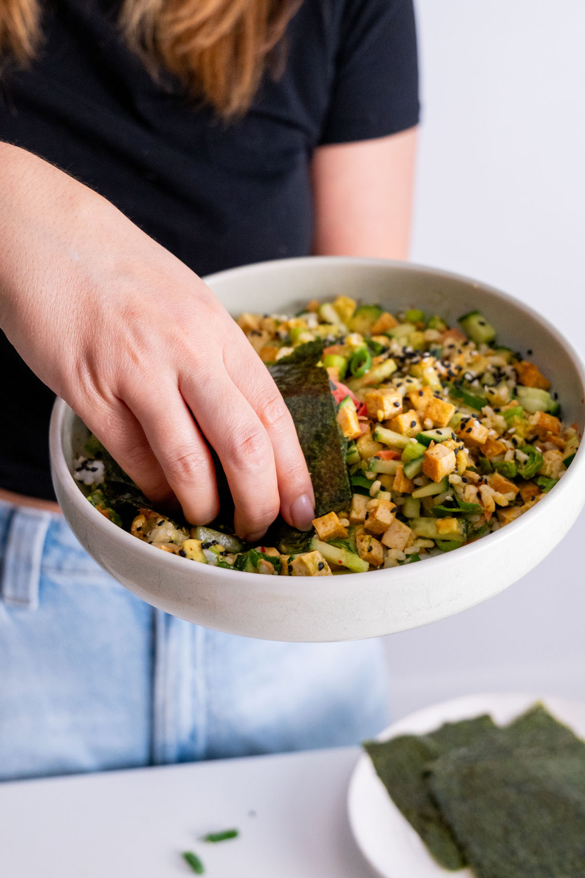 Sarah Cobacho holding a nori sheet over a sushi bowl, about to eat.
