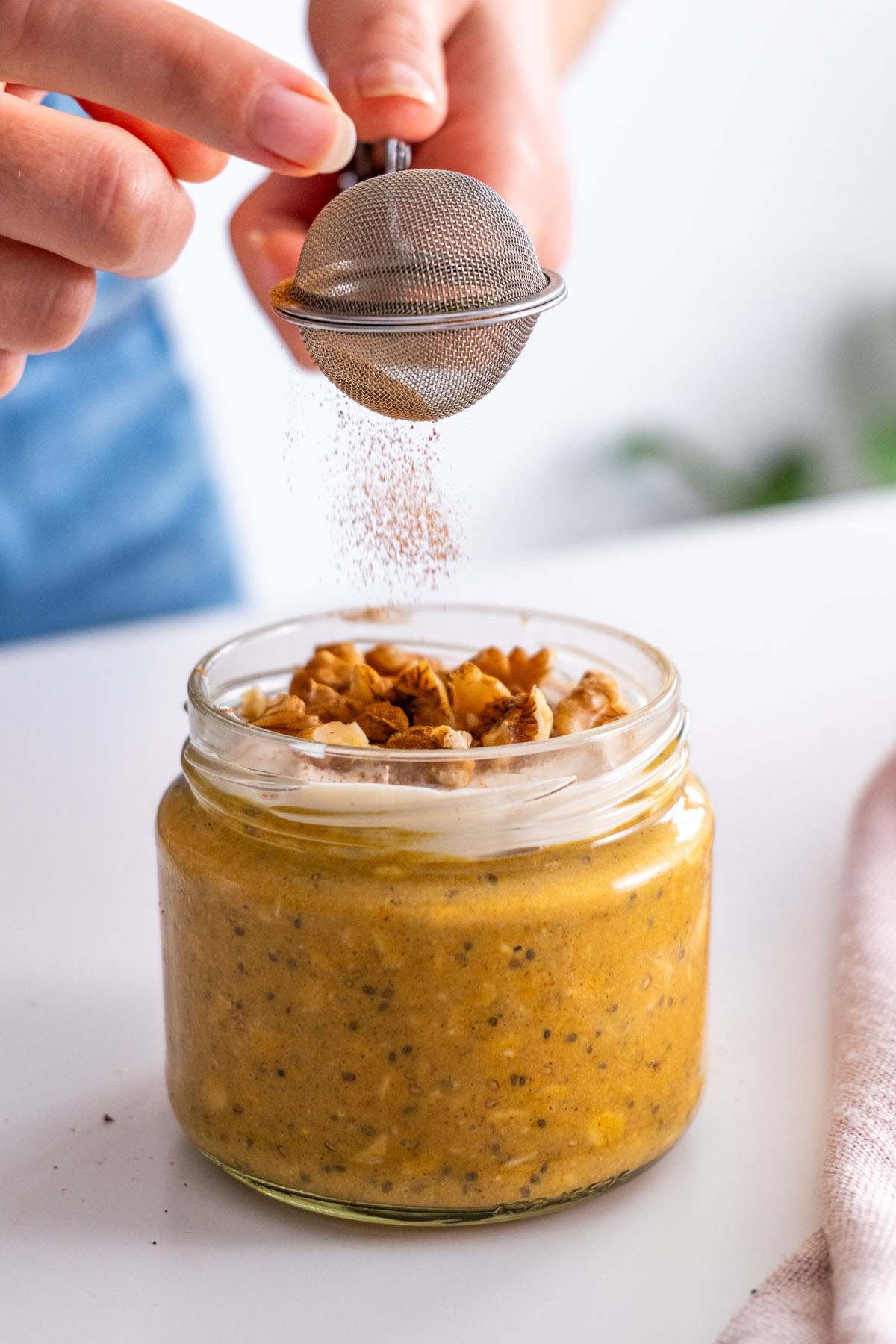 Close-up of Sarah Cobacho sprinkling cinnamon on pumpkin spice overnight oats