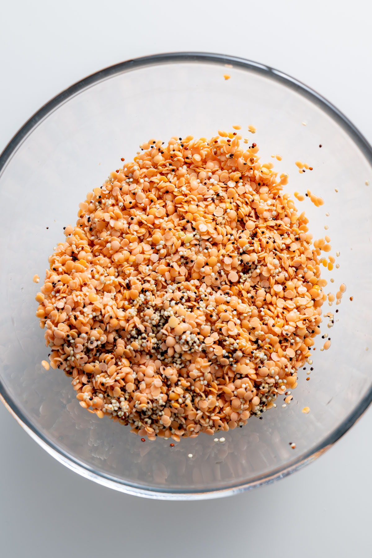 Close-up of soaked split red lentils and quinoa in a clear bowl.