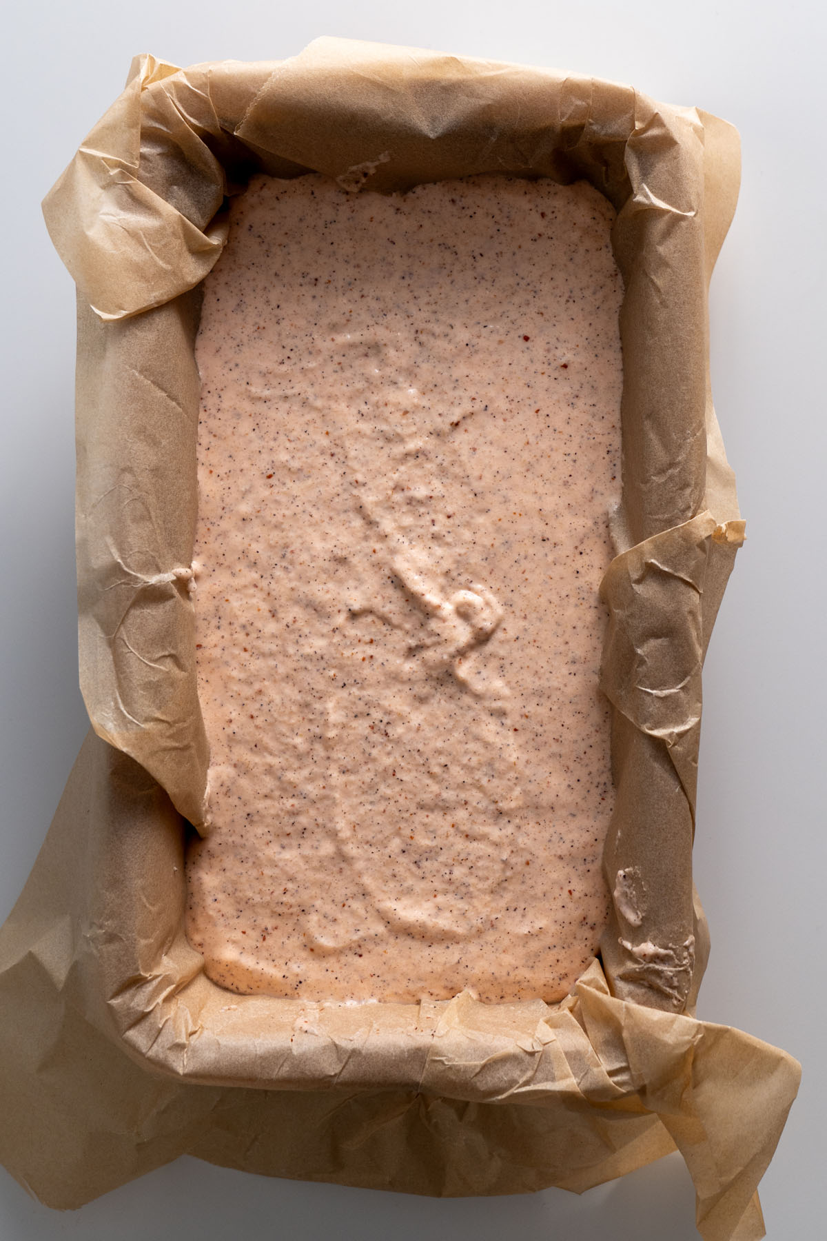 Red lentil quinoa bread batter spread in a parchment-lined loaf pan, ready to rise.