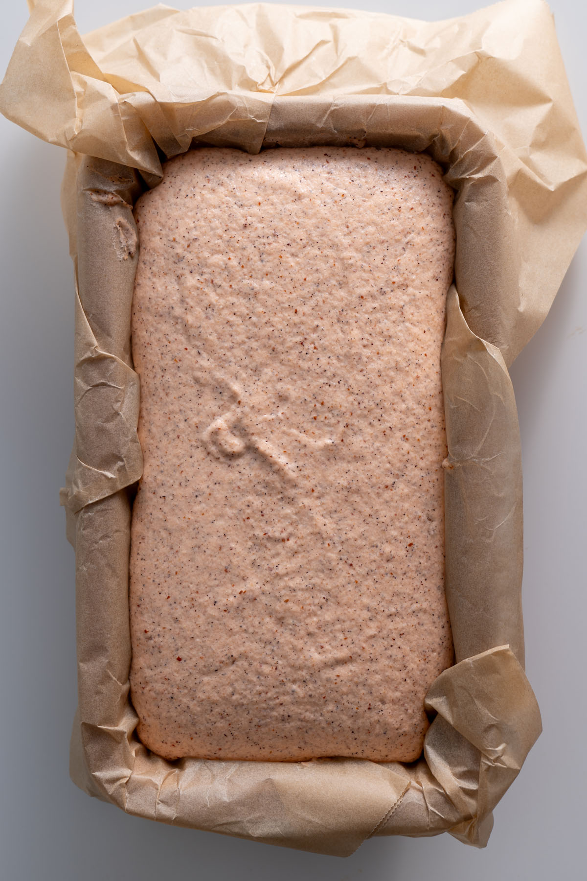 Red lentil quinoa bread batter rising in a parchment-lined loaf pan.