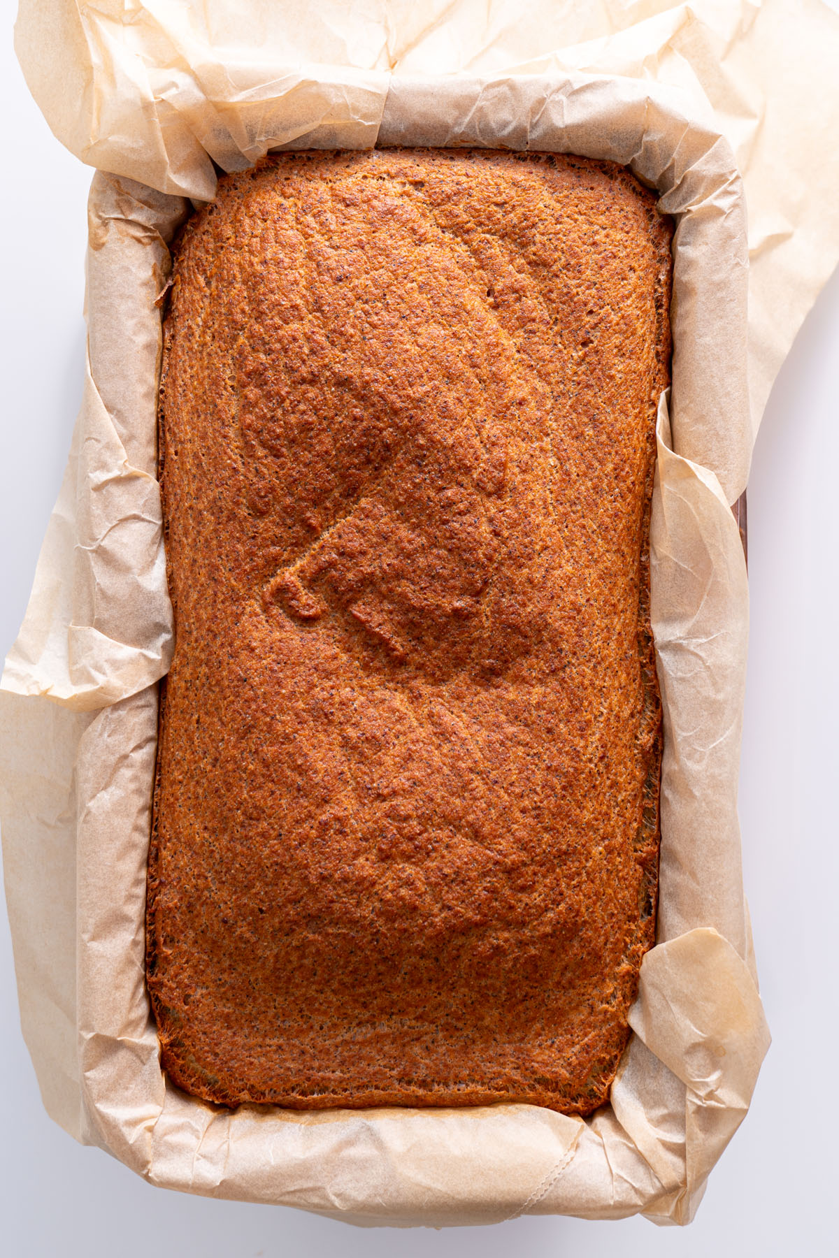 Baked red lentil quinoa bread in a parchment-lined loaf pan with a golden-brown crust.