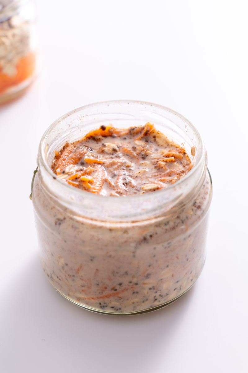 Jar of carrot cake overnight oats in the soaking phase, with oats and grated carrot visible in the mixture.