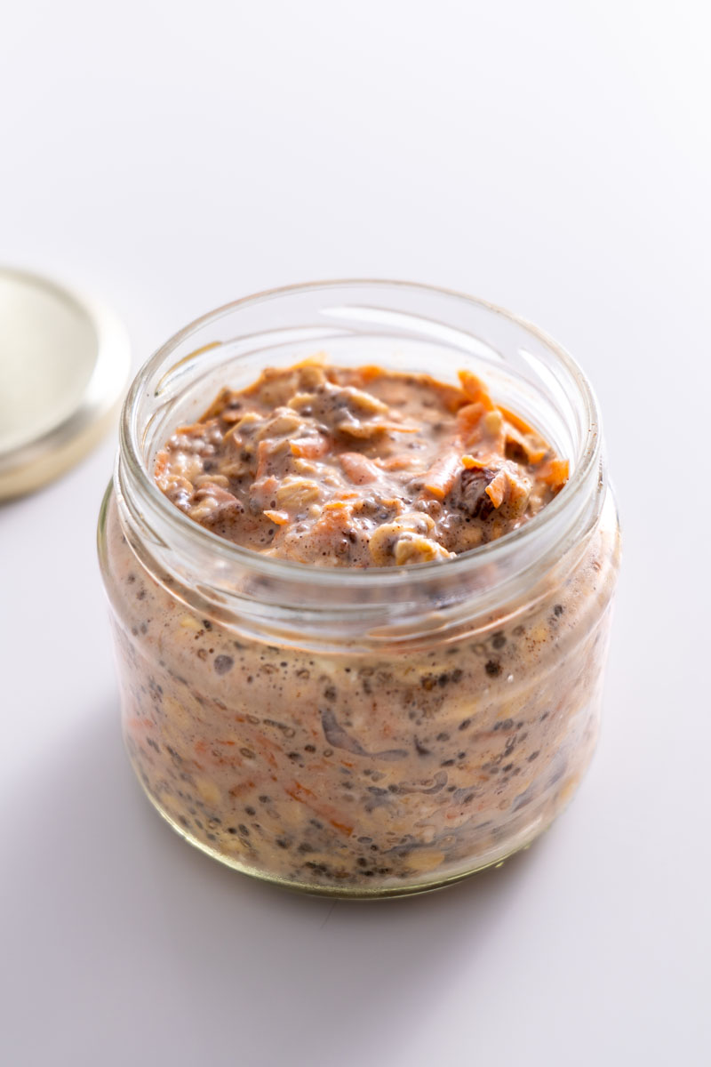 Jar of carrot cake overnight oats after soaking, showing a thick and well-mixed consistency with visible chia seeds and grated carrot.